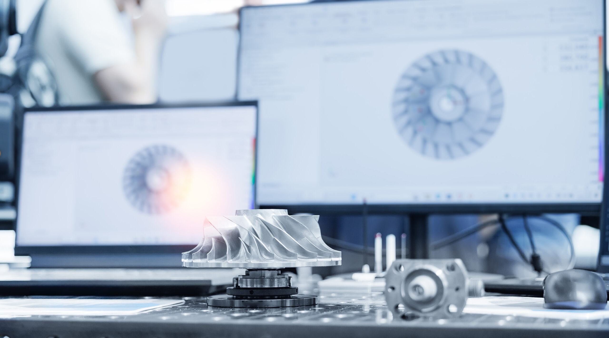 Cnc coordinate measuring machine with metal turbine prototype and cad monitors in workshop.